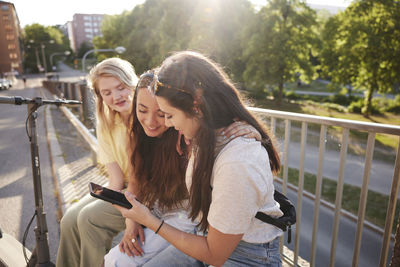 Young female friends spending time together outdoors and using phone