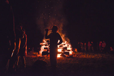 Silhouette people enjoying by bonfire on field against sky at night