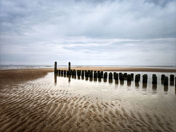 Wooden posts on beach against sky