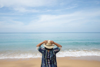 Rear view of woman touching hat while standing at beach