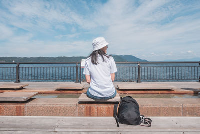 Rear view of woman sitting on railing against sky