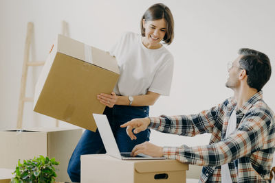 Man showing laptop to woman holding cardboard box