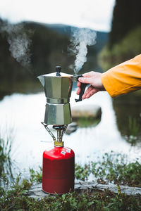 Cropped hand holding coffee maker on camping stove