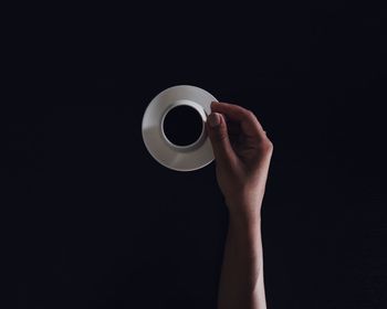 Cropped hand holding coffee cup on black background