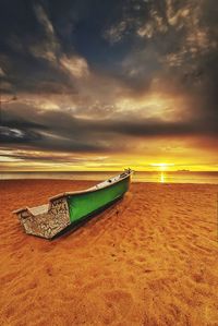 Boat moored on beach against sky during sunset