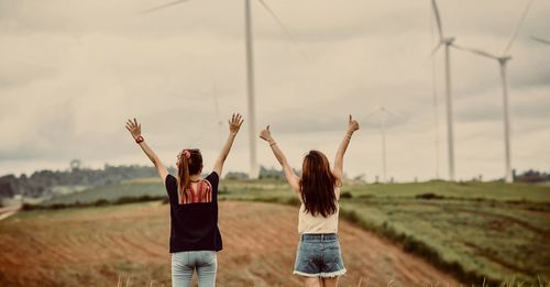 Rear view of women gesturing while standing on field against sky