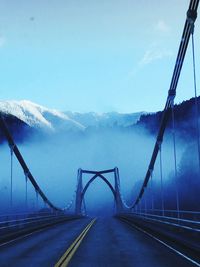 View of suspension bridge against snowcapped mountains