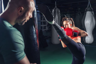 Young female boxer practicing with coach in gym