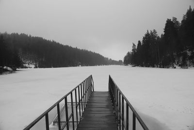 Footbridge on snow covered land against sky
