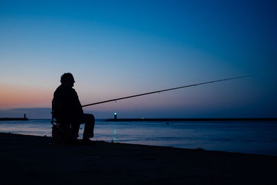 Silhouette man fishing in sea against blue sky during sunset