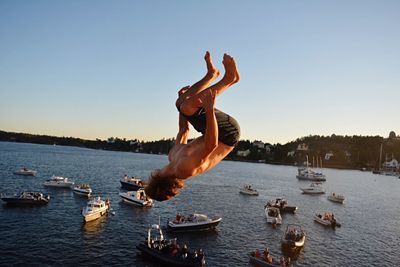 Side view of shirtless man in mid-air over sea against sky