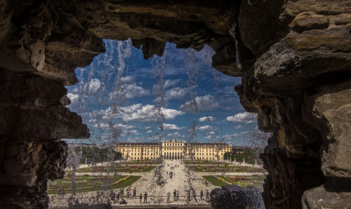 Building seen through water splashing from rock formation against sky