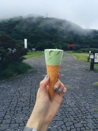 Close-up of hand holding ice cream against landscape