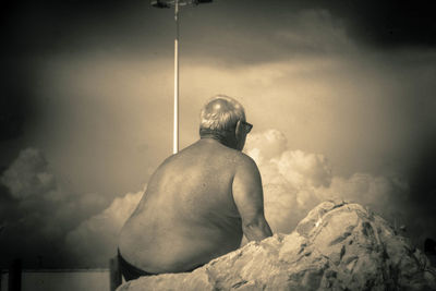 Rear view of shirtless man sitting against sky