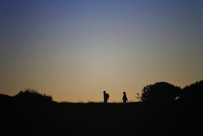 Silhouette people standing on landscape against clear sky during sunset