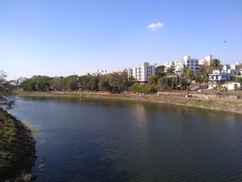 Scenic view of river by buildings against clear blue sky