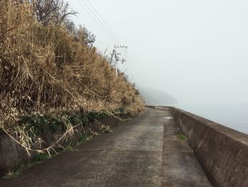 Surface level of empty road against clear sky in foggy weather