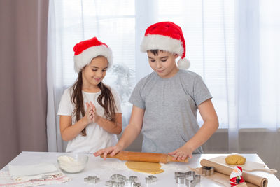 Children, brother and sister, in red caps, prepare christmas cookies in the kitchen