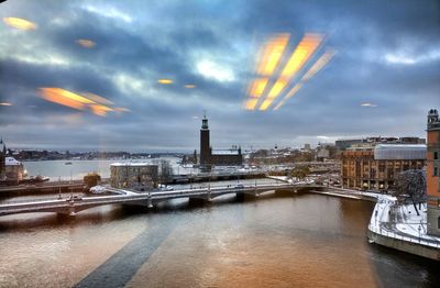 City at waterfront against cloudy sky