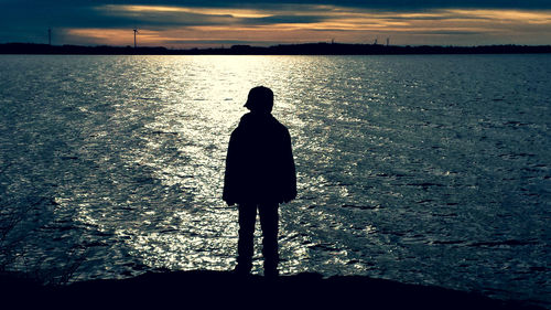 Rear view of silhouette man looking at sea against sunset sky