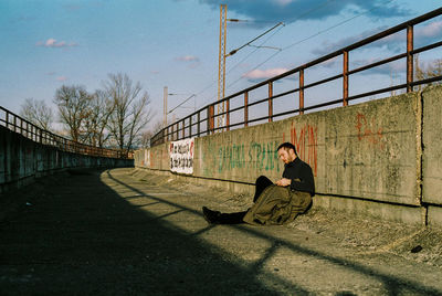 Man sitting on bridge against sky