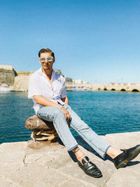 Man sitting on chair by sea against clear sky