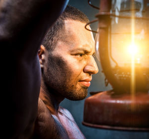 Shirtless muscular worker holding lantern against wall