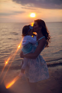 Mother holding her child girl at sunset by the sea