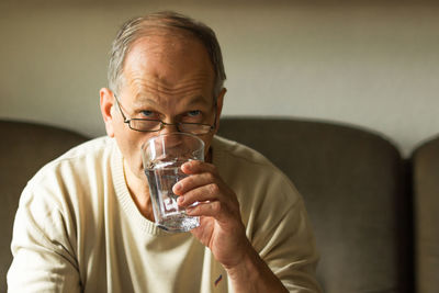 Caucasian senior man take capsule and drinking water from glass on sofa at home, feels like sick.