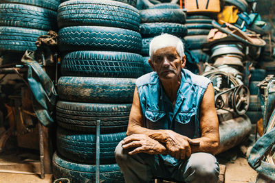 Portrait of man sitting by tires at garage