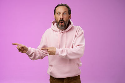 Portrait of young man standing against pink background