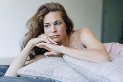 A beautiful red-haired woman lying on the bed leans on the pillows and looks thoughtfully away.