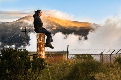 Full length side view of man sitting on metallic rod against mountain