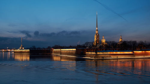 Illuminated building by river against sky