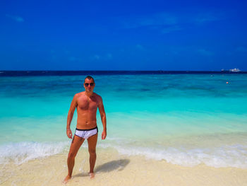 Full length of shirtless man standing at beach against sky