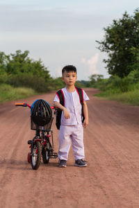 Full length of boy standing by bicycle on road against sky
