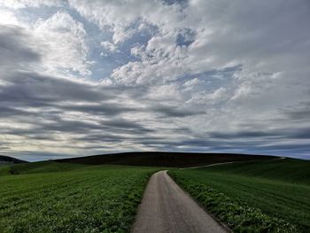 Empty road amidst field against sky