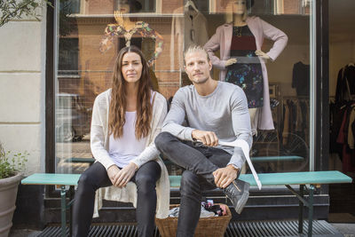 Portrait of owner with female worker sitting in front of clothing store