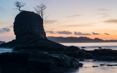 Rocks on shore against sky during sunset