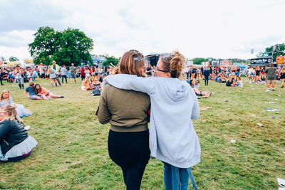 Rear view of friends walking on grass in musical festival