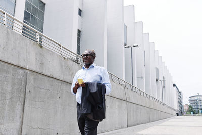 Businessman with mobile phone and blazer walking in city