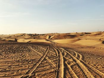 Tire tracks on desert against sky