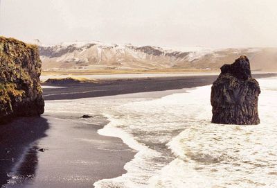 Sea by mountain against sky during winter