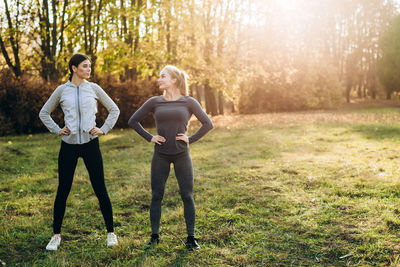 Two girlfriends are doing exercises in nature, looking at each other.