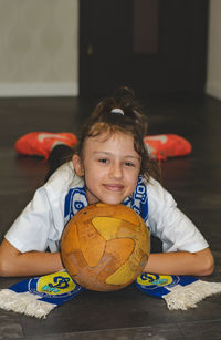 The girl is lying on the floor with a fan scarf and a ball under her face.