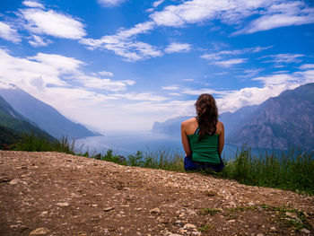 Rear view of man sitting on mountain against sky