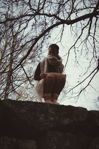 Woman sitting on rock against bare tree