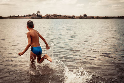 Rear view of shirtless man in sea against sky