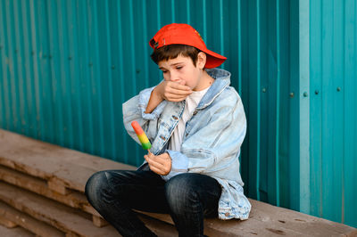 Boy in a red cap  crying against the background of a blue wall. he holds colorful ice cream