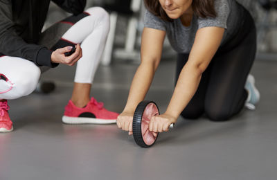 Low section of instructor assisting woman in exercising at gym